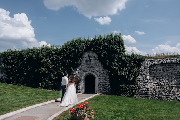Hermosa vista posterior de una pareja casada frente a la entrada en el muro de piedra al aire libre