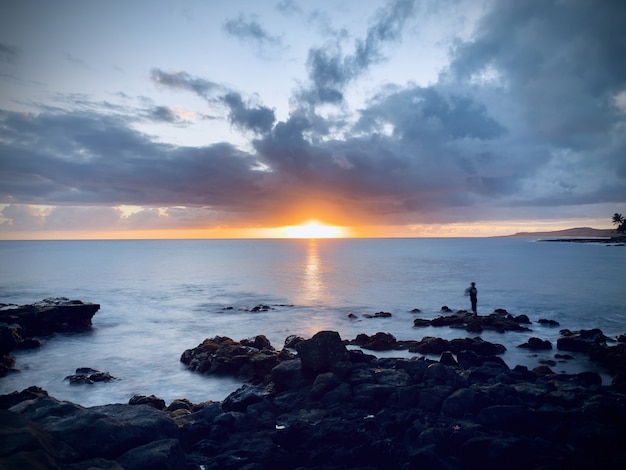 Hermosa vista de la puesta de sol en el cielo nublado sobre el océano tranquilo en la costa rocosa