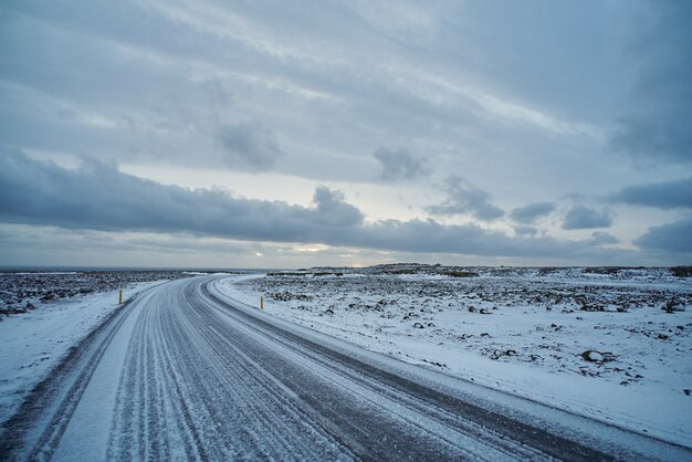 Hermosa vista sobre la carretera congelada vacía con hielo en islandia. océano lejano, nubes en el cielo, clima invernal desagradable