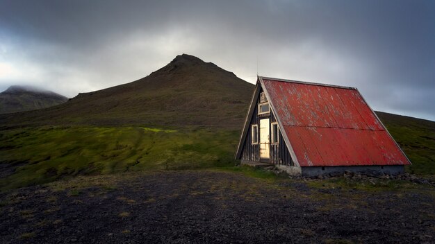 Hermosa vista de una vieja casa roja aislada en medio de un campo verde junto a las montañas