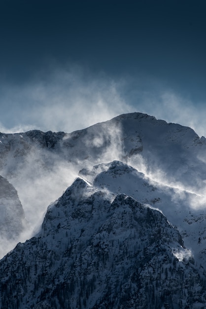 Hermosas altas montañas nevadas y neblinosas con nieve soplada por el viento