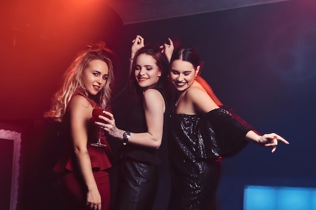 Hermosas amigas elegantemente vestidas se divierten en la discoteca, bailando en la pista de baile con alcohol.