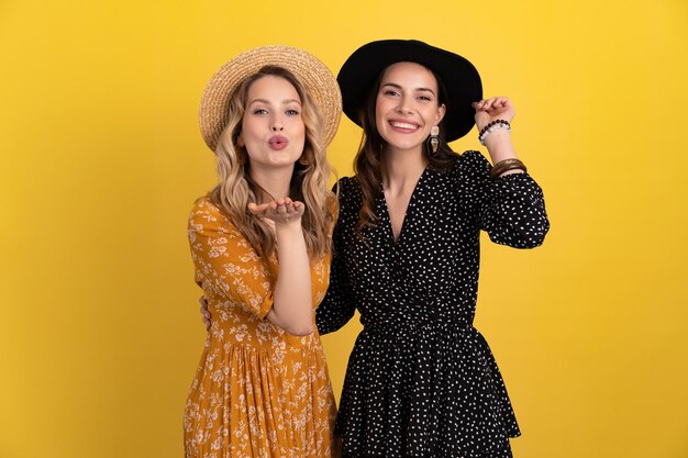 Hermosas amigas juntas aisladas de fondo amarillo con vestido y sombrero negros y amarillos