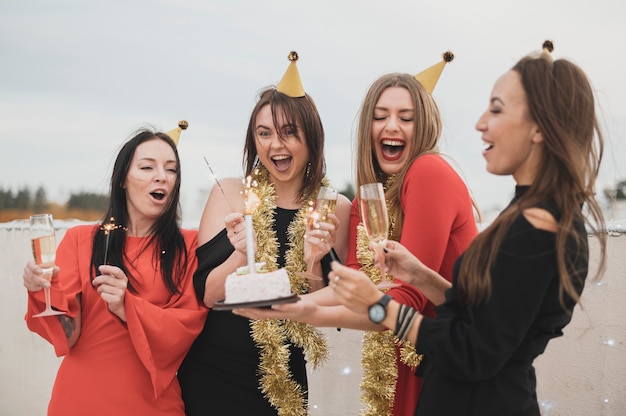 Hermosas chicas sosteniendo el pastel de cumpleaños en una fiesta en la azotea