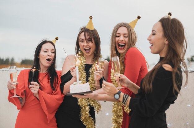 Hermosas chicas sosteniendo el pastel de cumpleaños en una fiesta en la azotea