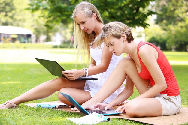 Hermosas chicas usando computadoras portátiles en un parque