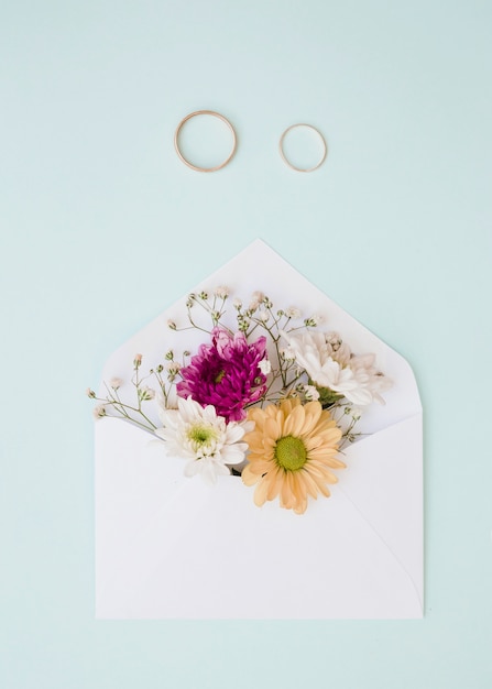 Hermosas flores dentro del sobre blanco con dos anillos de boda sobre fondo azul