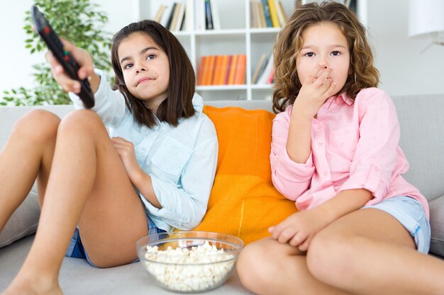 Hermosas hermanas jóvenes comiendo palomitas de maíz en casa.