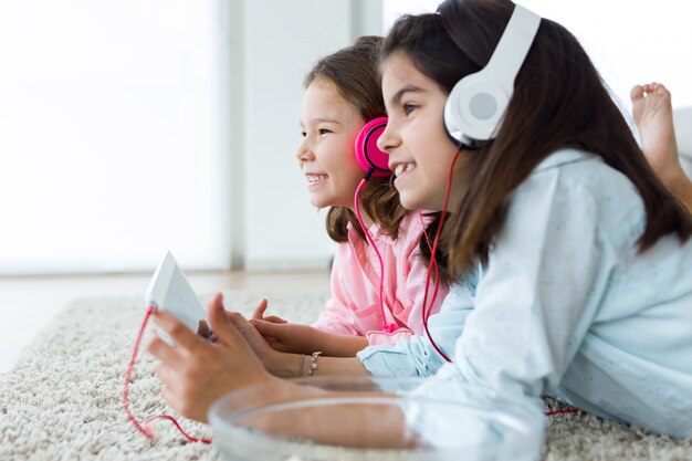 Hermosas jóvenes hermanas escuchando música con tableta digital a