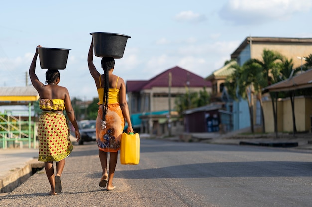 Foto gratuita hermosas mujeres africanas a buscar agua desde el exterior