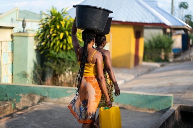 Foto gratuita hermosas mujeres africanas a buscar agua desde el exterior