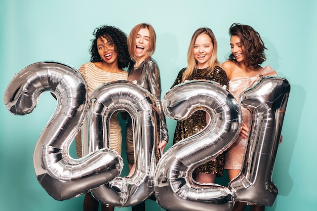 Hermosas mujeres celebrando el año nuevo.Feliz mujer hermosa en elegantes vestidos de fiesta sexy sosteniendo globos plateados 2021, divirtiéndose en la fiesta de fin de año. Celebración navideña