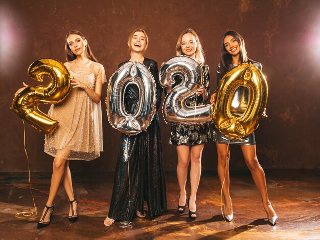 Hermosas mujeres celebrando año nuevo. Niñas hermosas y felices con elegantes vestidos de fiesta sexys con globos dorados y plateados 2020, divirtiéndose en la fiesta de fin de año. Celebración navideña Modelos encantadores