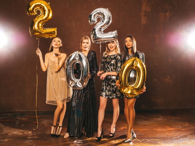 Hermosas mujeres celebrando año nuevo. Niñas hermosas y felices con elegantes vestidos de fiesta sexys con globos dorados y plateados 2020, divirtiéndose en la fiesta de fin de año. Celebración navideña Modelos encantadores