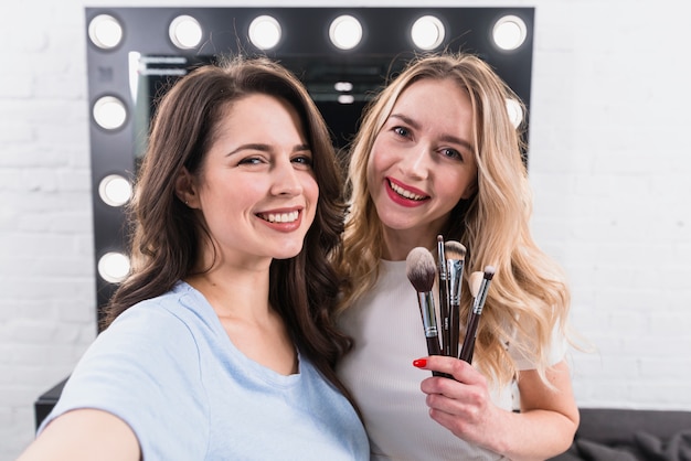 Hermosas mujeres sonrientes con pinceles tomando selfie