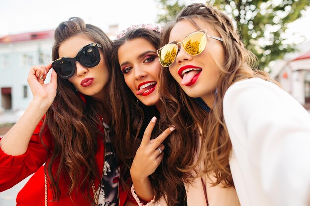 Hermosas novias con gafas de sol mostrando signos de paz a la cámara con una sonrisa.