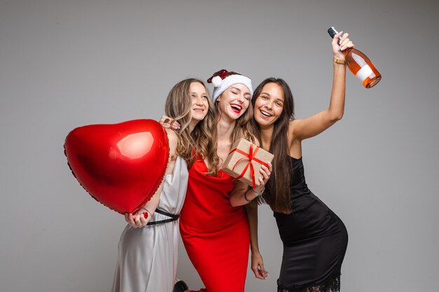 Hermosas novias con globo de corazón, botella de vino y presente.