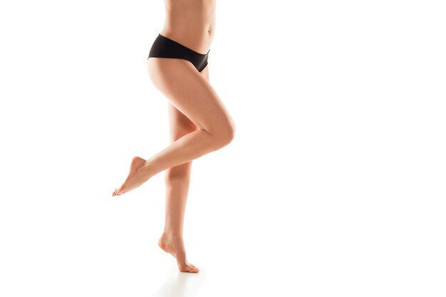 Hermosas piernas femeninas, glúteos y vientre aislados en la pared blanca. Concepto de belleza, cosmética, spa, depilación, tratamiento y fitness. Cuerpo en forma y deportivo, sensual con piel cuidada en ropa interior.