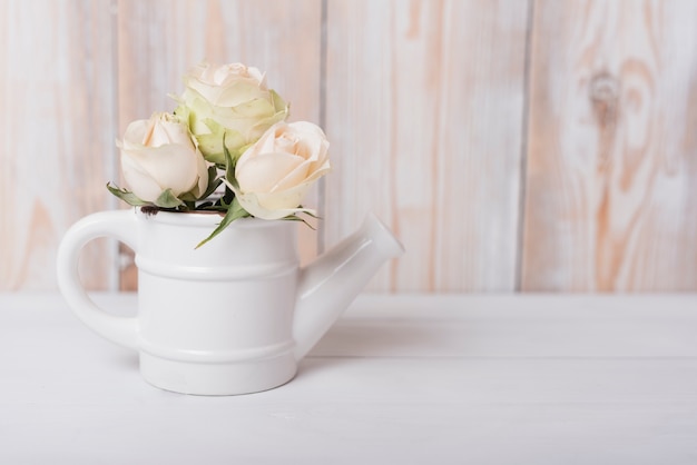 Hermosas rosas en la pequeña regadera de cerámica en mesa de madera.