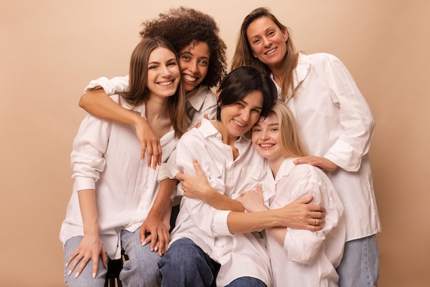 Foto gratuita hermosas señoritas diversas en jeans y camisas blancas miran a la cámara sobre fondo beige concepto del día de la mujer