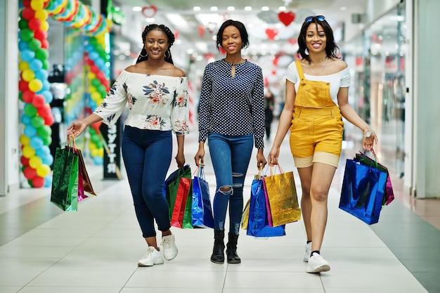 Hermosas tres chicas afroamericanas bien vestidas con bolsas de compras de colores caminando en el centro comercial