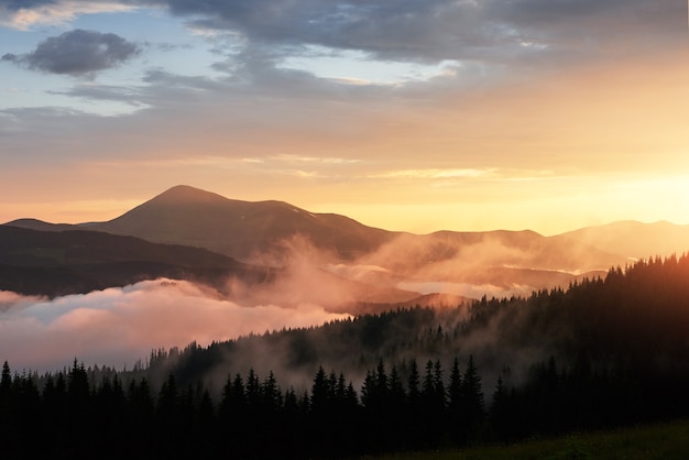 Hermoso atardecer en las montañas. Paisaje con luz del sol brillando a través de nubes naranjas y niebla.