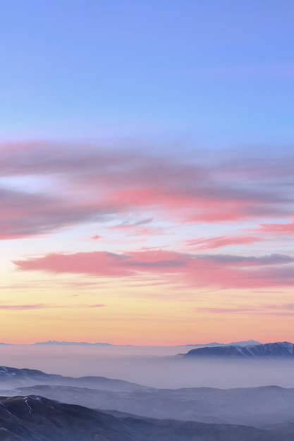 Hermoso atardecer pastel sobre montañas rocosas cubiertas por la nube