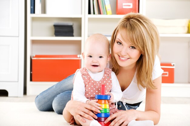 Hermoso bebé jugando con juguetes con madre feliz en el interior