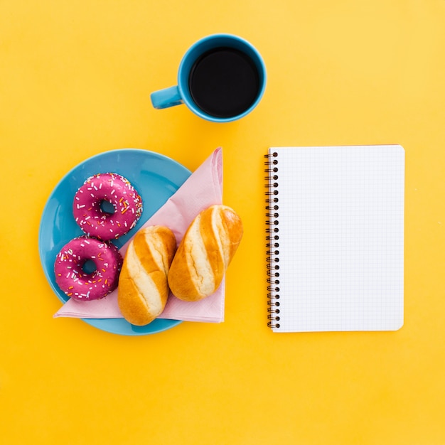 Hermoso desayuno con donas y taza de café con cuaderno en amarillo