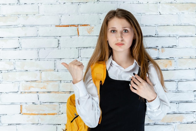 Hermoso estudiante en uniforme se para sobre fondo blanco y señala el pulgar a un lado Foto de alta calidad