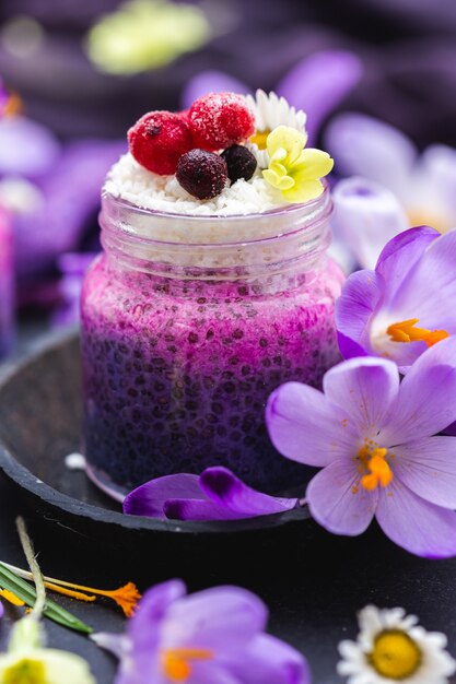 Hermoso frasco de batido vegano púrpura cubierto con bayas, rodeado de flores de primavera