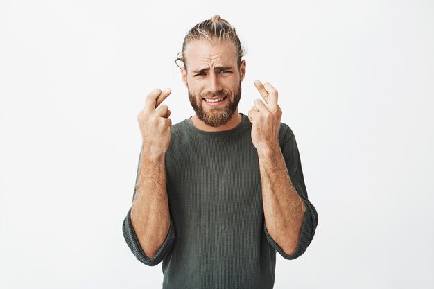 Hermoso hombre sin afeitar con los dedos cruzados con expresión preocupada