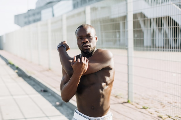 Hermoso hombre afroamericano hace estiramientos antes de un entrenamiento fuera