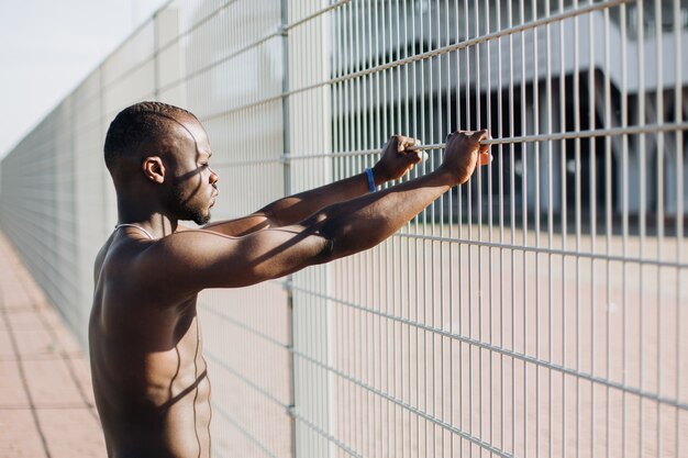 Hermoso hombre afroamericano hace estiramientos antes de un entrenamiento fuera