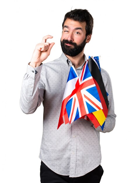 Hermoso hombre con barba sosteniendo muchas banderas y haciendo signo minúsculo