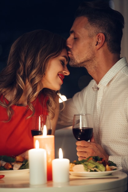Hermoso hombre besando a su sonriente mujer feliz mientras cena romántica