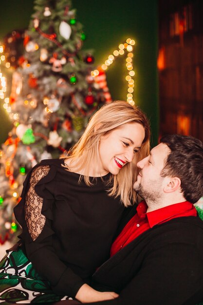 Hermoso hombre y mujer disfrutan el tiempo sentado en una silla suave antes de un árbol de Navidad