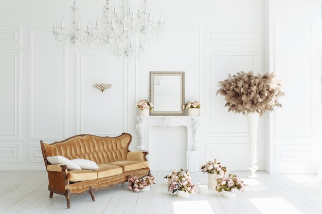 Hermoso interior blanco clásico con una chimenea, un sofá marrón y una lámpara de araña vintage.