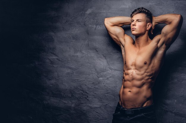Hermoso modelo de hombre joven sin camisa con buen cuerpo musculoso posando en un estudio. Aislado en un fondo oscuro.