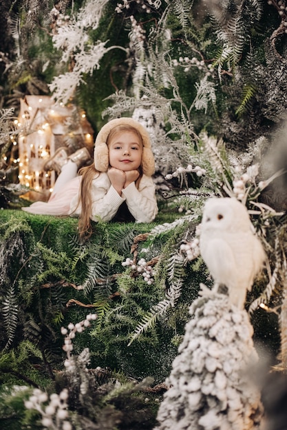 Hermoso niño caucásico con cabello largo rubio se encuentra en un ambiente navideño con muchos árboles decorados a su alrededor y búho