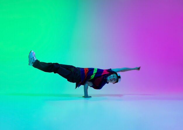 Hermoso niño deportivo bailando hip-hop con ropa elegante en la pared degradada de colores en el salón de baile con luz de neón. Cultura juvenil, movimiento, estilo y moda, acción. Retrato brillante de moda.