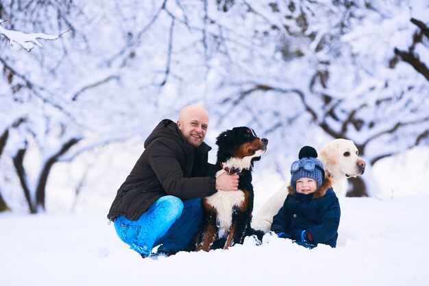 El hermoso padre, hijo y perros sentados en la nieve