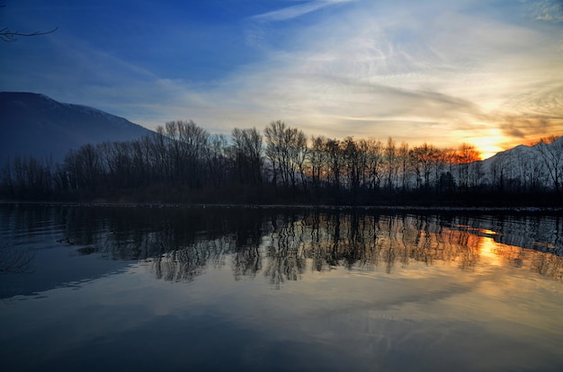 Hermoso paisaje al atardecer sobre el lago con siluetas de árboles reflejados en el agua