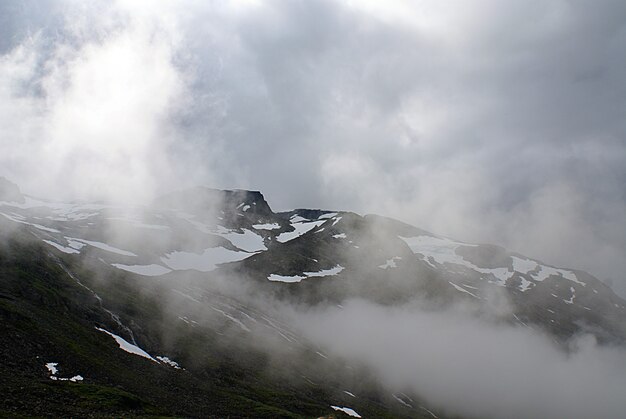 Hermoso paisaje de altas montañas rocosas cubiertas de nieve envuelta en niebla en Noruega