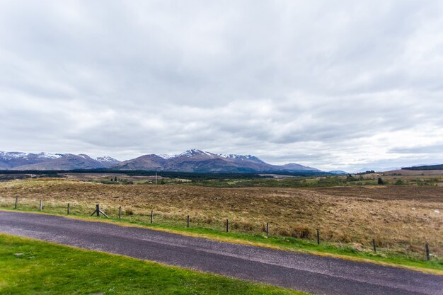 Hermoso paisaje con una carretera y altas montañas cubiertas de nieve reluciente bajo el cielo nublado