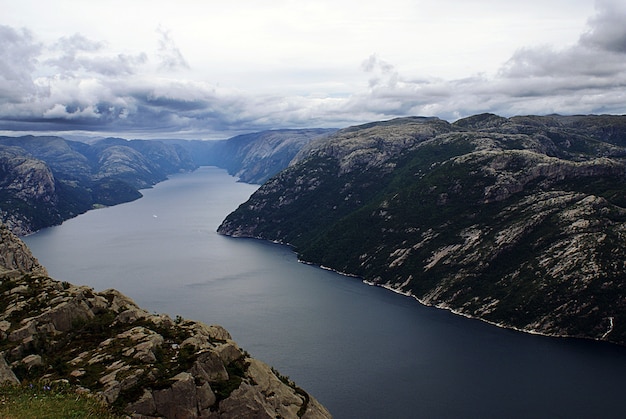 Foto gratuita hermoso paisaje de los famosos acantilados de preikestolen cerca de un lago bajo un cielo nublado en stavanger, noruega