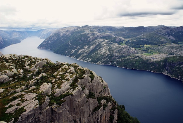 Foto gratuita hermoso paisaje de los famosos acantilados de preikestolen cerca de un río bajo un cielo nublado en stavanger, noruega