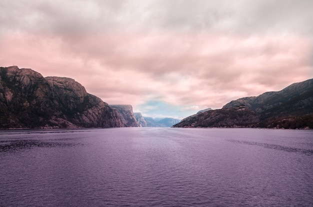 Hermoso paisaje del mar rodeado de altas formaciones rocosas bajo las nubes de tormenta en Noruega