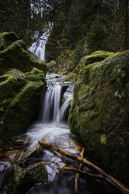 Hermoso paisaje de una poderosa cascada en un bosque cerca de formaciones rocosas cubiertas de musgo