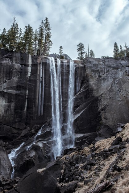 Hermoso paisaje de una poderosa cascada que fluye a través de un acantilado rocoso bajo un cielo nublado